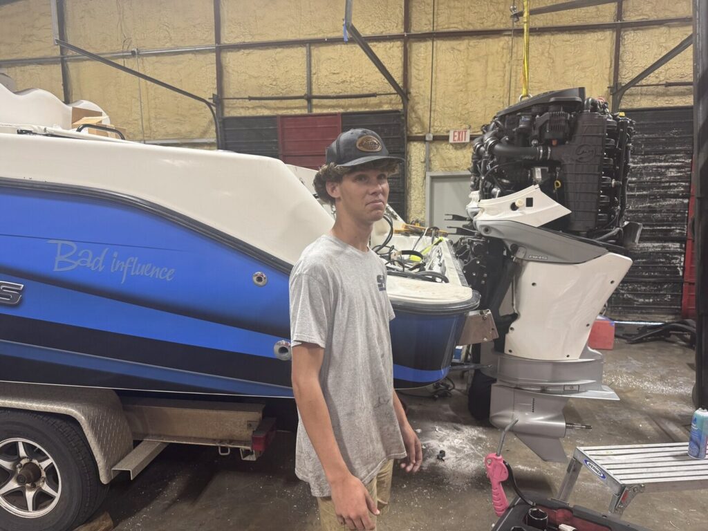 Student in a marine service shop beside a boat
