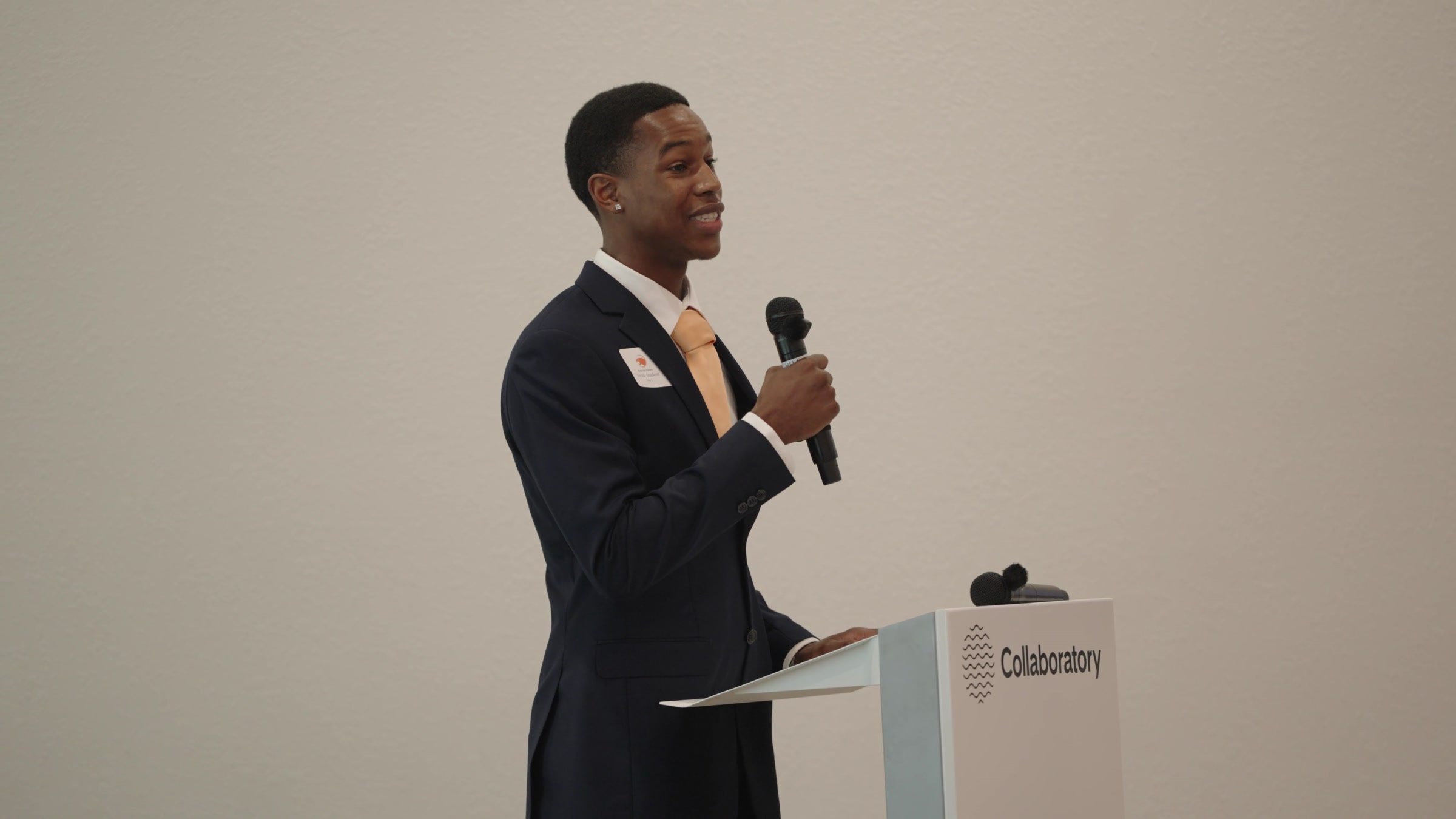 STEMCAT student in a suit speaking at the podium during a community event